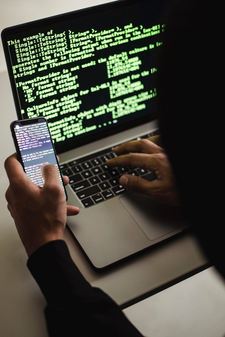 A person using a smartphone beside a laptop showing lines of code