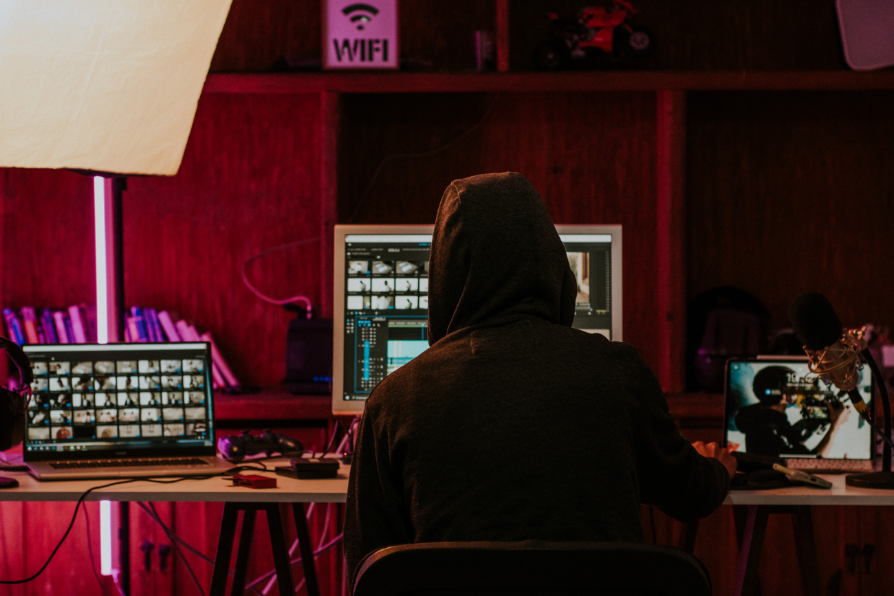 A hooded figure working at computers under a Wi-Fi sign