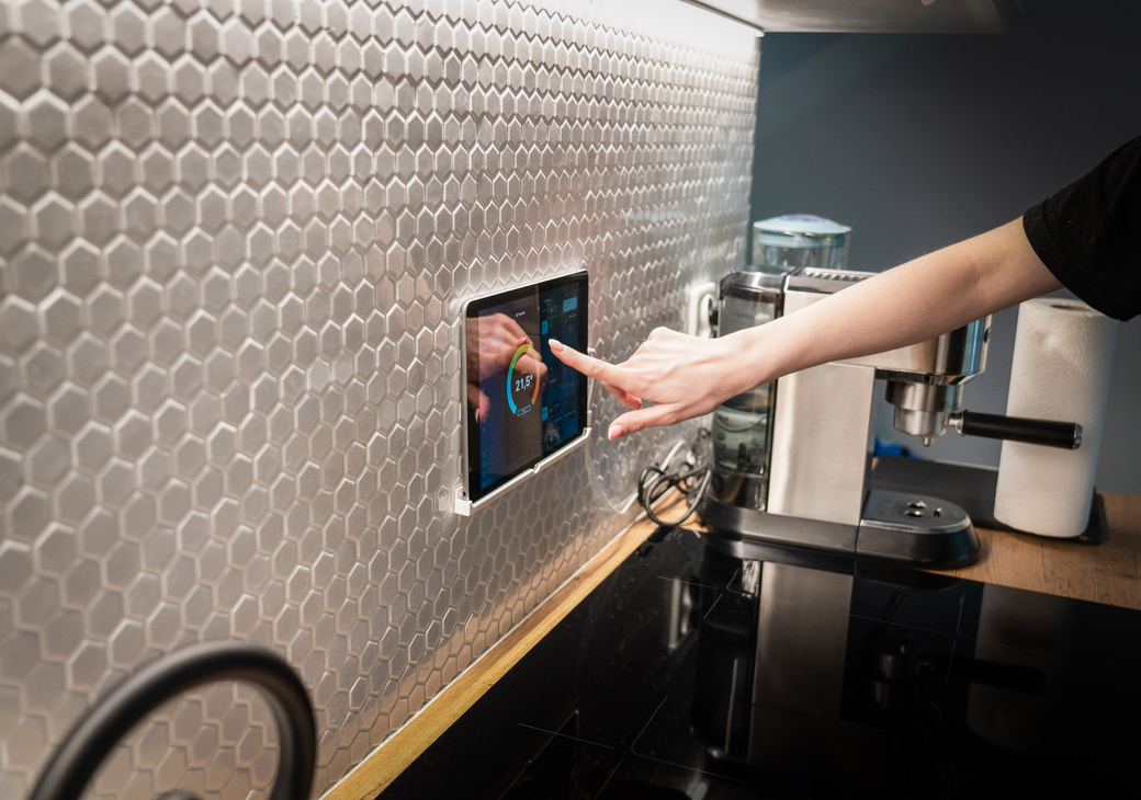 A hand tapping a wall-mounted smart touchscreen panel